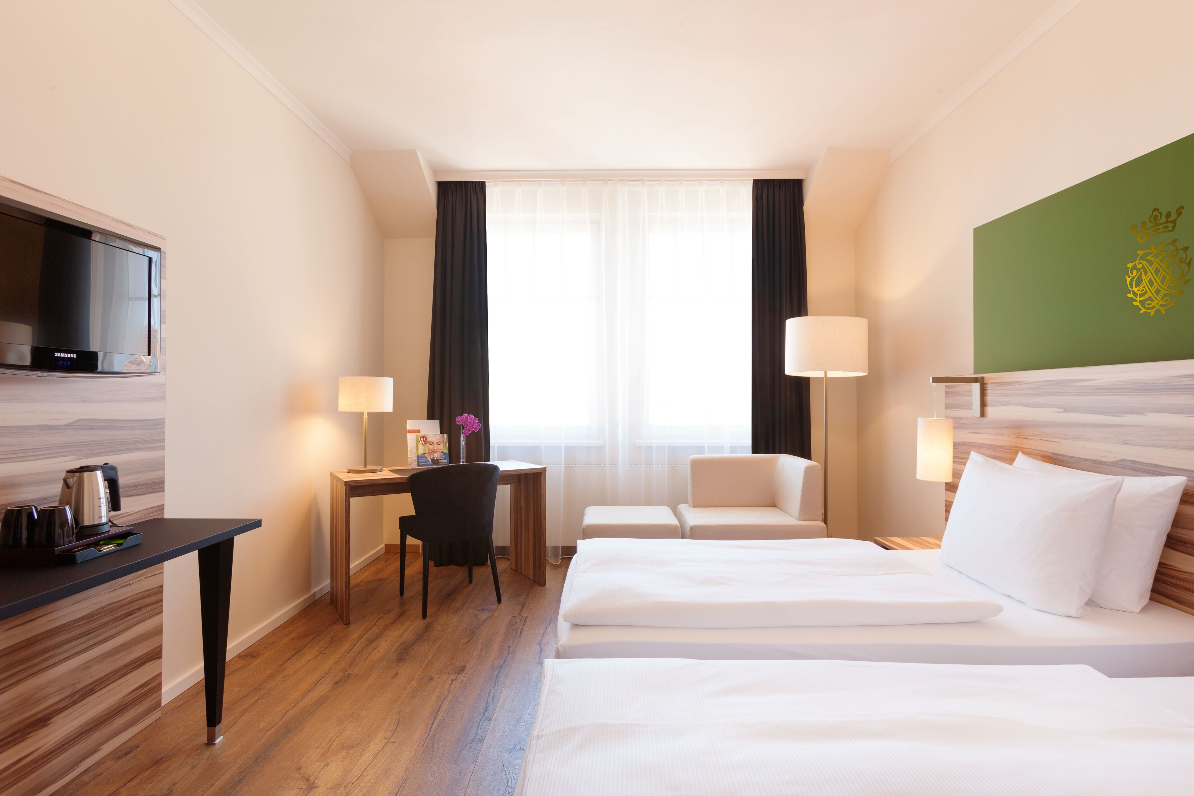 Ein Hotelzimmer mit einem Bett, einem Schreibtisch, einem Sessel, einem Fernseher und einem Fenster mit Vorhängen.