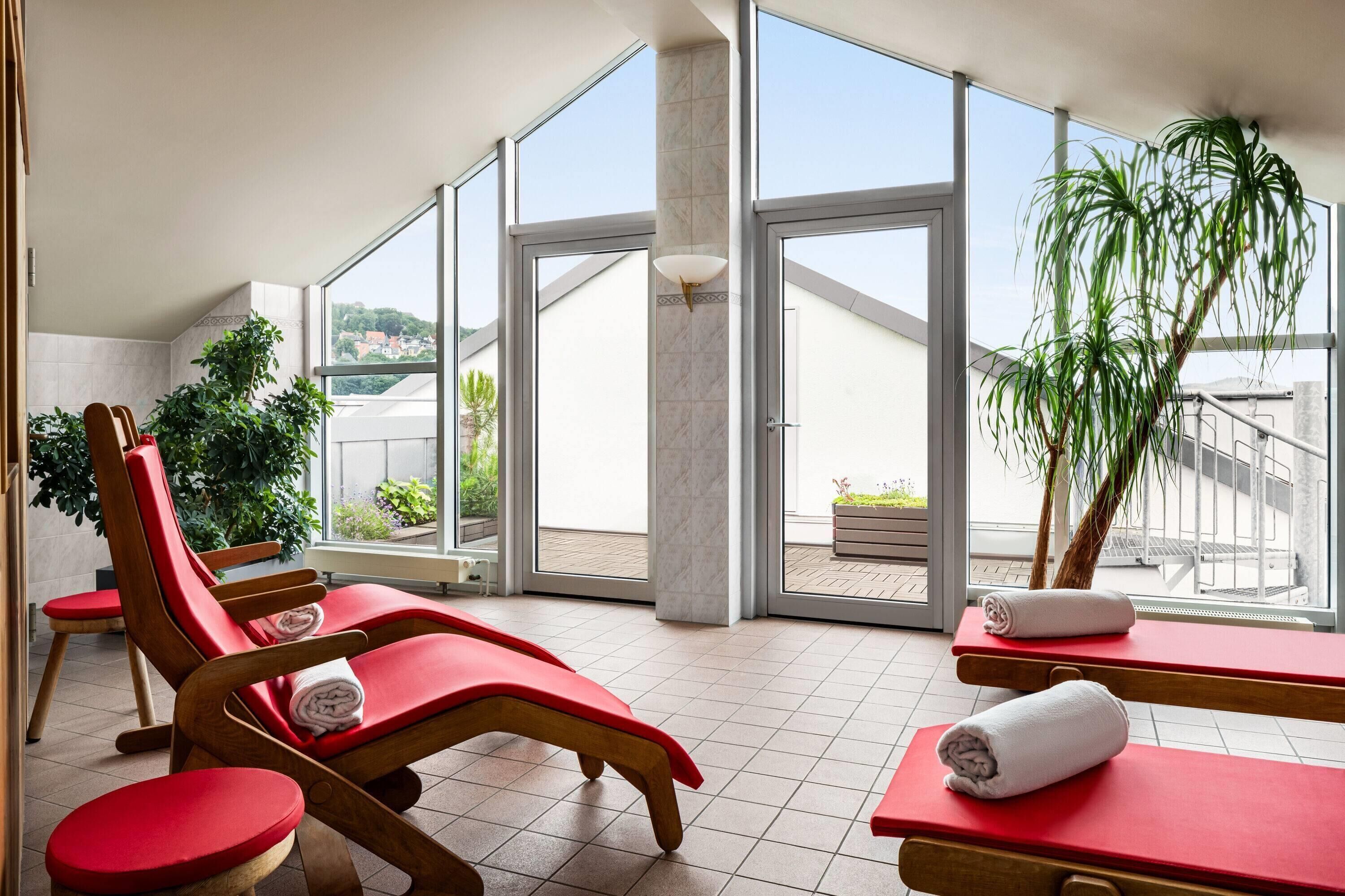 Zona de spa con tumbonas rojas, una planta en maceta y vistas al exterior.