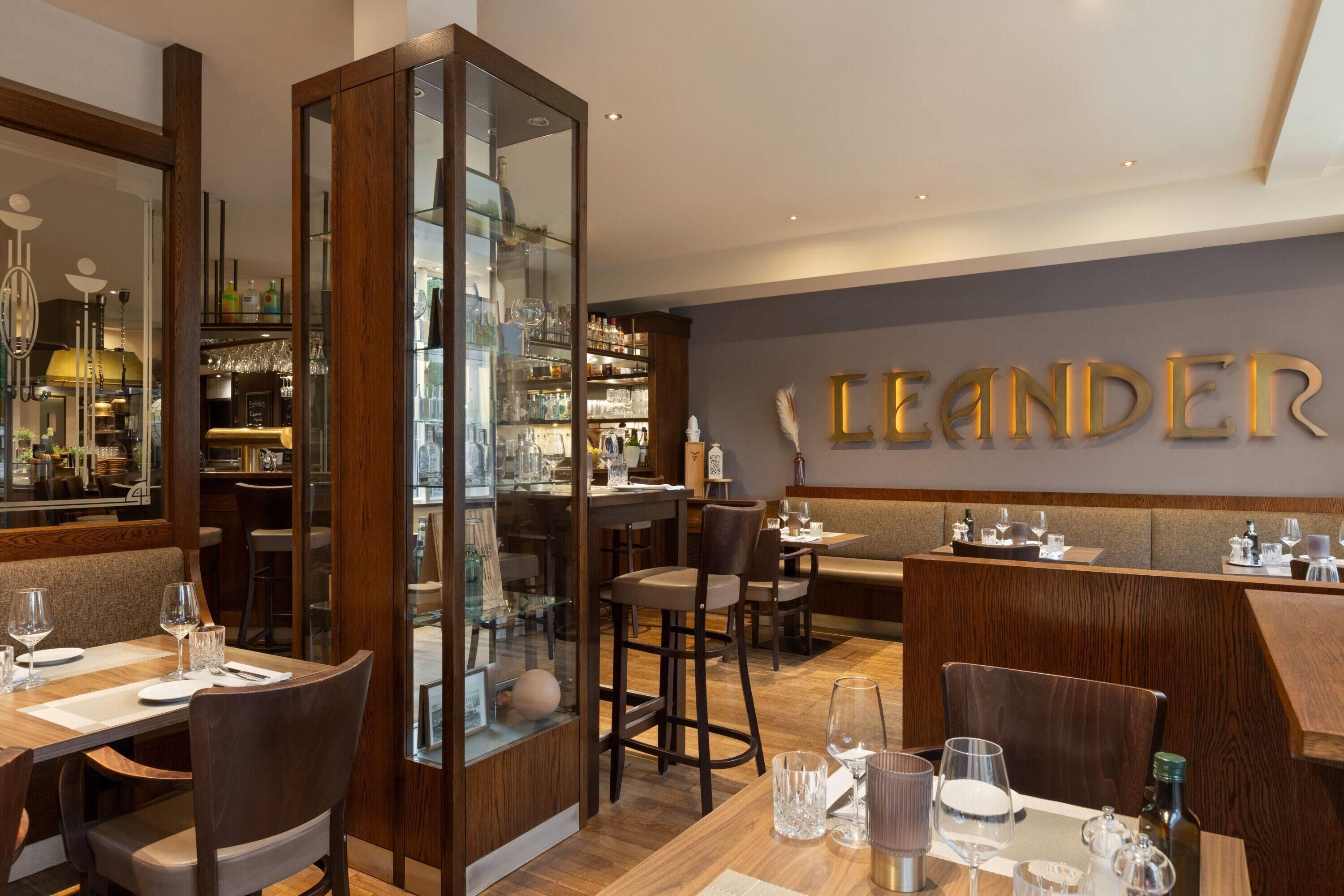 Restaurante com área de bar, móveis de madeira e parede com o nome 'LEANDER'.