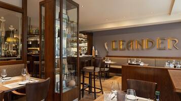 Restaurante com área de bar, móveis de madeira e parede com o nome 'LEANDER'.