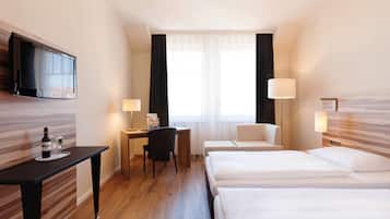 Une chambre d’hôtel équipée d’une télévision à écran plat, d’un bureau avec une chaise, de deux lits et d’une grande fenêtre avec des rideaux.