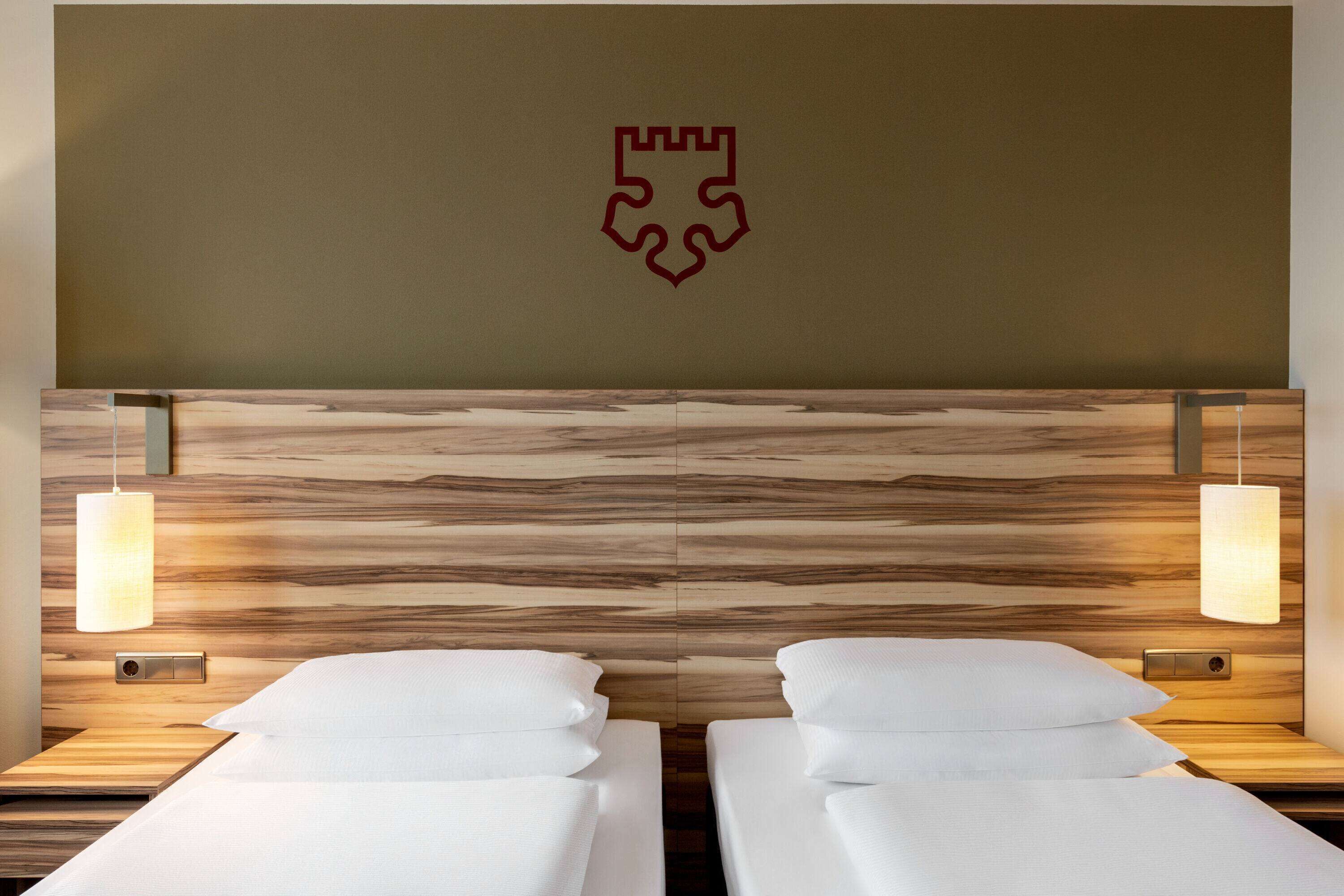 A hotel room with a wooden headboard, two beds with white linens, and bedside lamps.