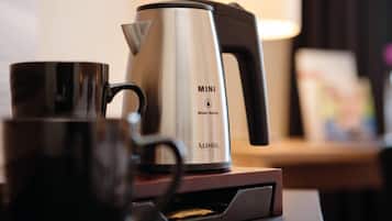 A stainless steel mini water-saving coffee maker with a black handle, placed on a wooden surface.