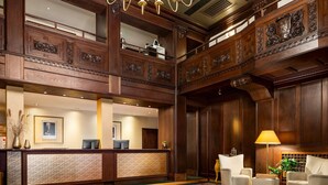Un vestíbulo de hotel con una recepción, dos sillones, una lámpara y un espejo grande.