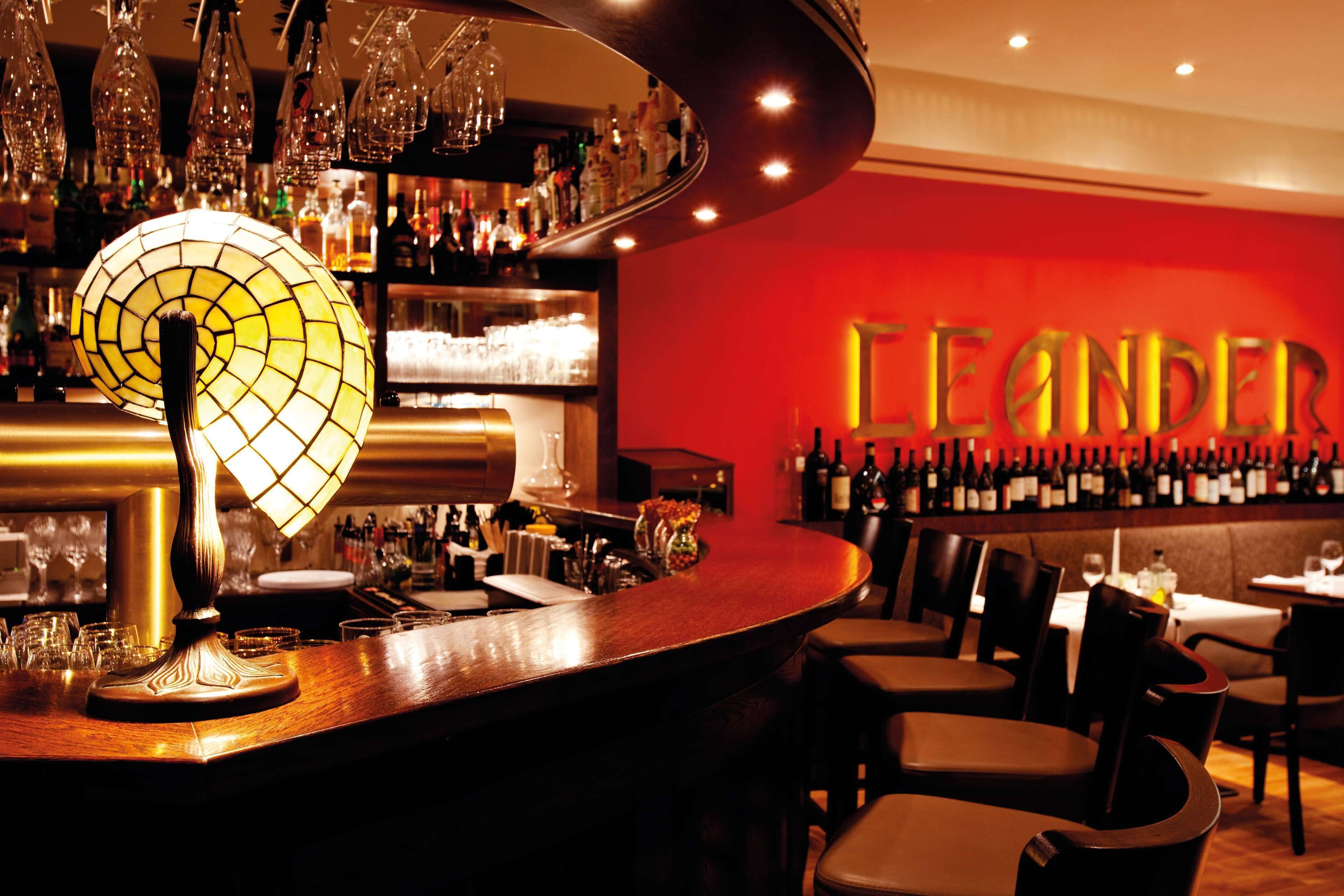 Una zona de bar con una mesa redonda, sillas y una pared con botellas.