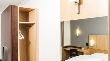 Een hotelkamer met een houten garderobe, een bed, een bureau met stoel en een telefoon aan de muur.
