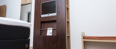 A room with a bed, a small desk with a monitor, and a bench.