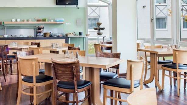 A modern restaurant with wooden tables and chairs, a kitchen area, and large windows. - Good Morning Erfurt (Erfurt)