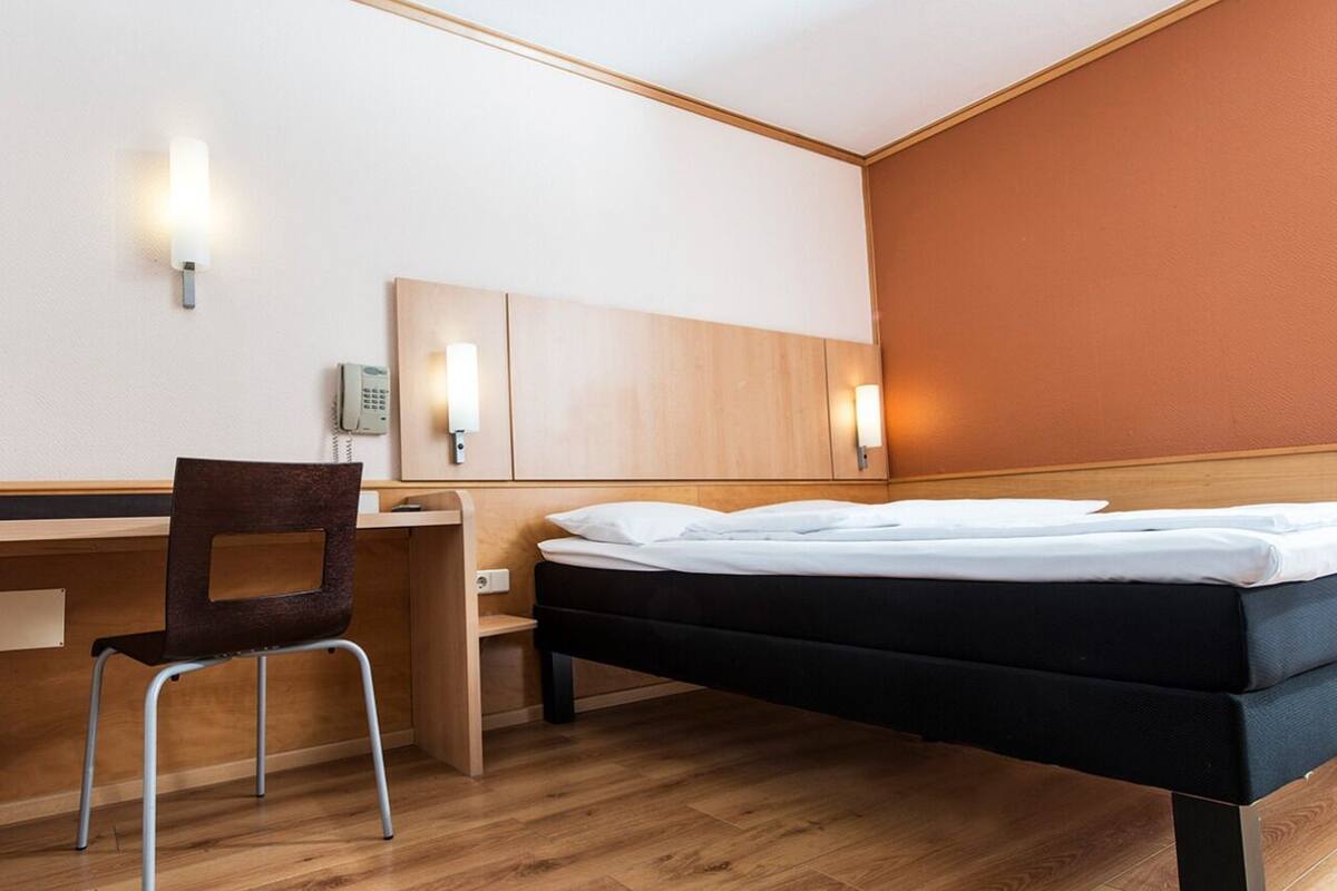 A hotel room with a bed, a desk, a chair, and a phone.