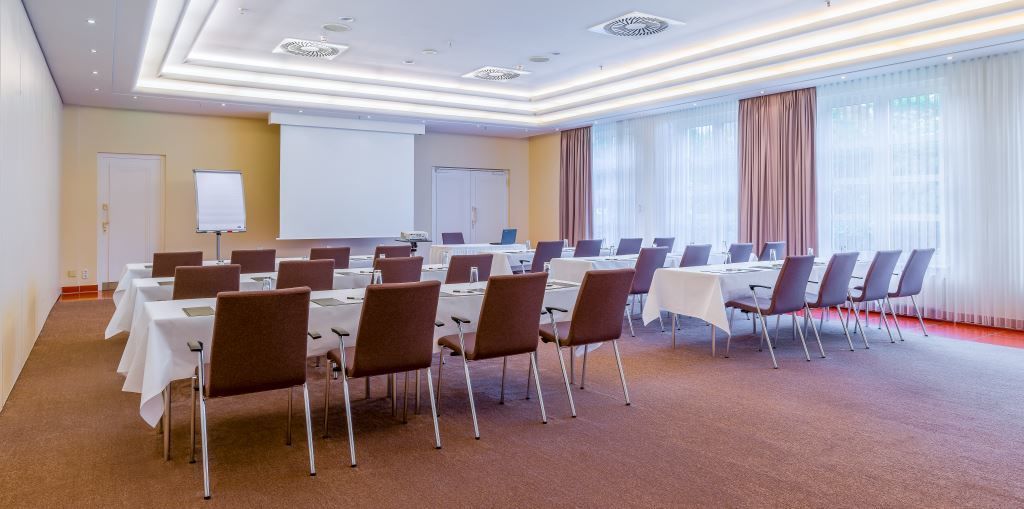 A conference room with multiple tables and chairs, a whiteboard, and a projector screen.