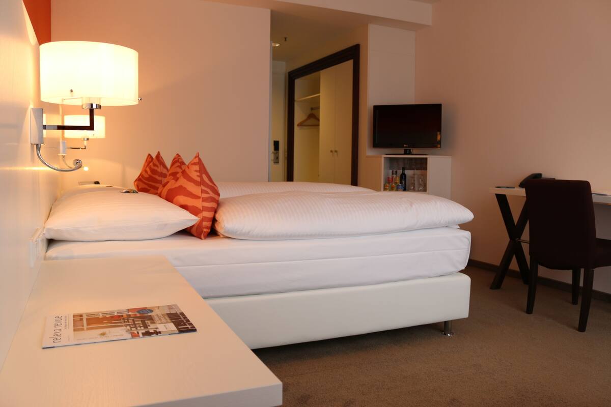 A hotel room with a bed, a desk, a chair, a TV, and a lamp.