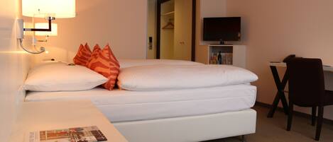 A hotel room with a bed, a desk, a chair, a TV, and a lamp.