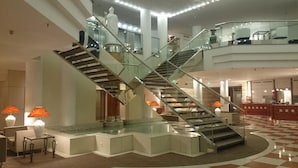 Eine moderne Hotelhalle mit einer zentralen Glasstiege, einem Empfangsbereich und Sitzbereichen.