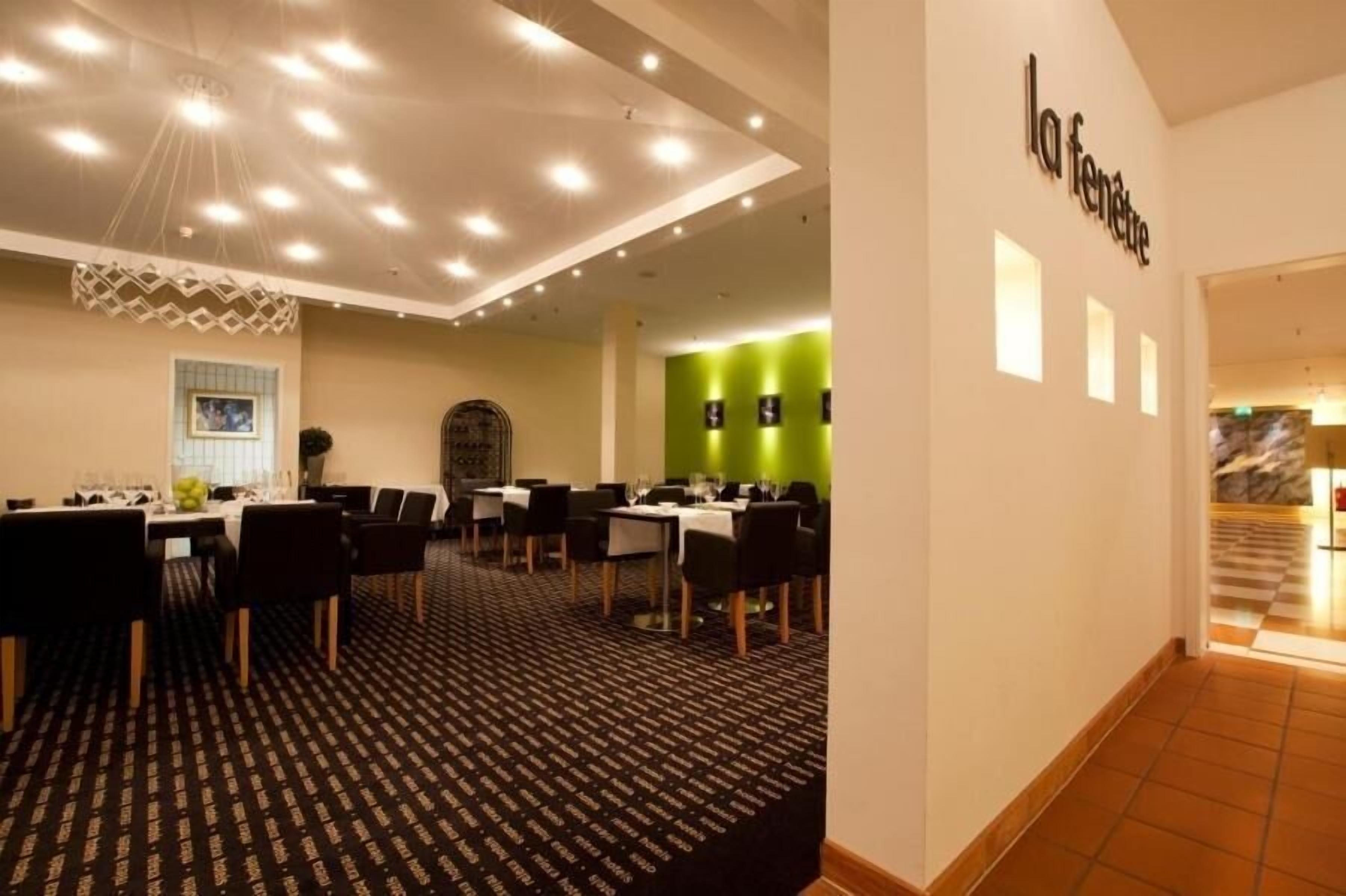 Un vestíbulo de hotel con varias mesas y sillas de comedor, una alfombra estampada y una pared verde de acento.