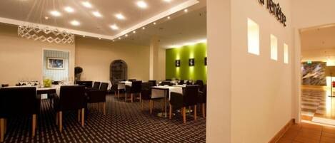 Un vestíbulo de hotel con varias mesas y sillas de comedor, una alfombra estampada y una pared verde de acento.