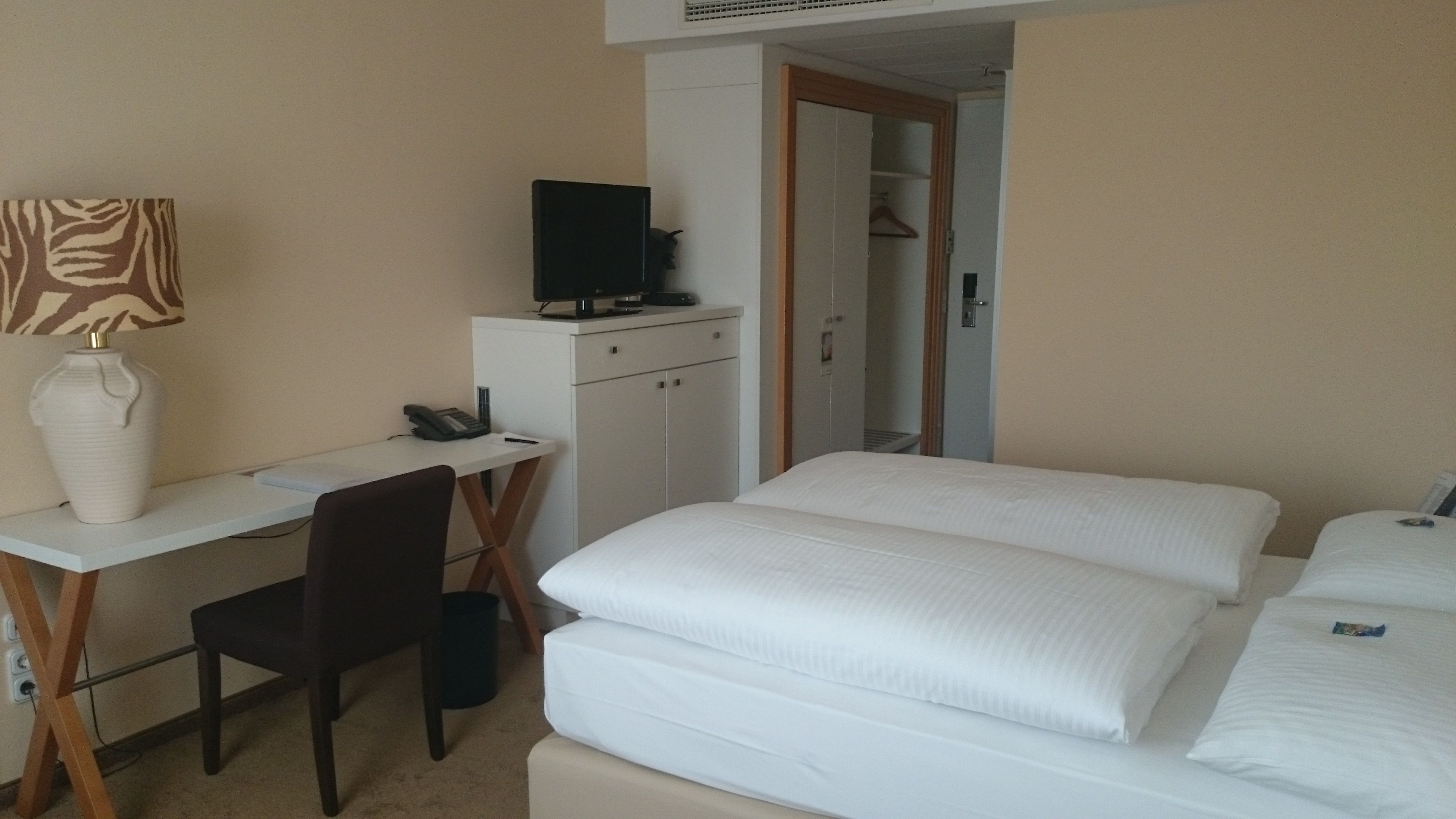Una habitación de hotel con escritorio, silla, dos camas, televisor y armario.