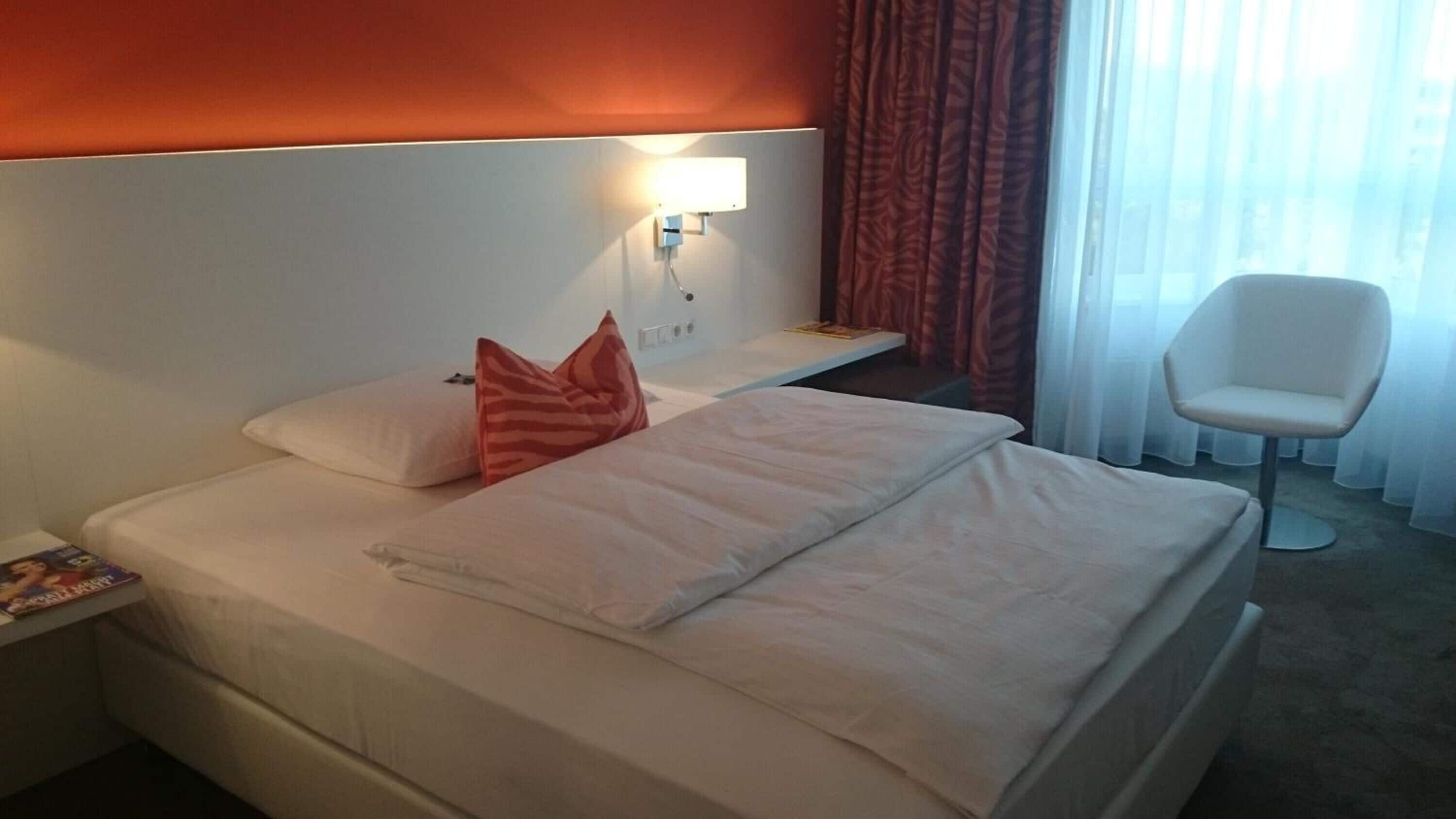 Una habitación de hotel con una cama, una mesita de noche, una silla y una ventana con cortinas.