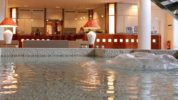 Ein Empfangsbereich mit Rezeptionstresen, einer Sitzecke und einem Pool mit Wasserspiel.