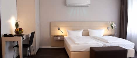 A hotel room with a bed, bedside tables, a desk, a chair, an air conditioner, and a window with curtains.