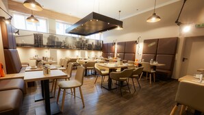 A modern restaurant interior with multiple dining tables and chairs, wooden flooring, and pendant lighting. - Manhattan Hotel (Frankfurt)