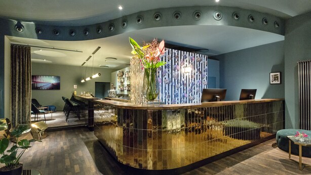 A reception area with a curved counter, seating, and a decorative vase. - Manhattan Hotel (Frankfurt)
