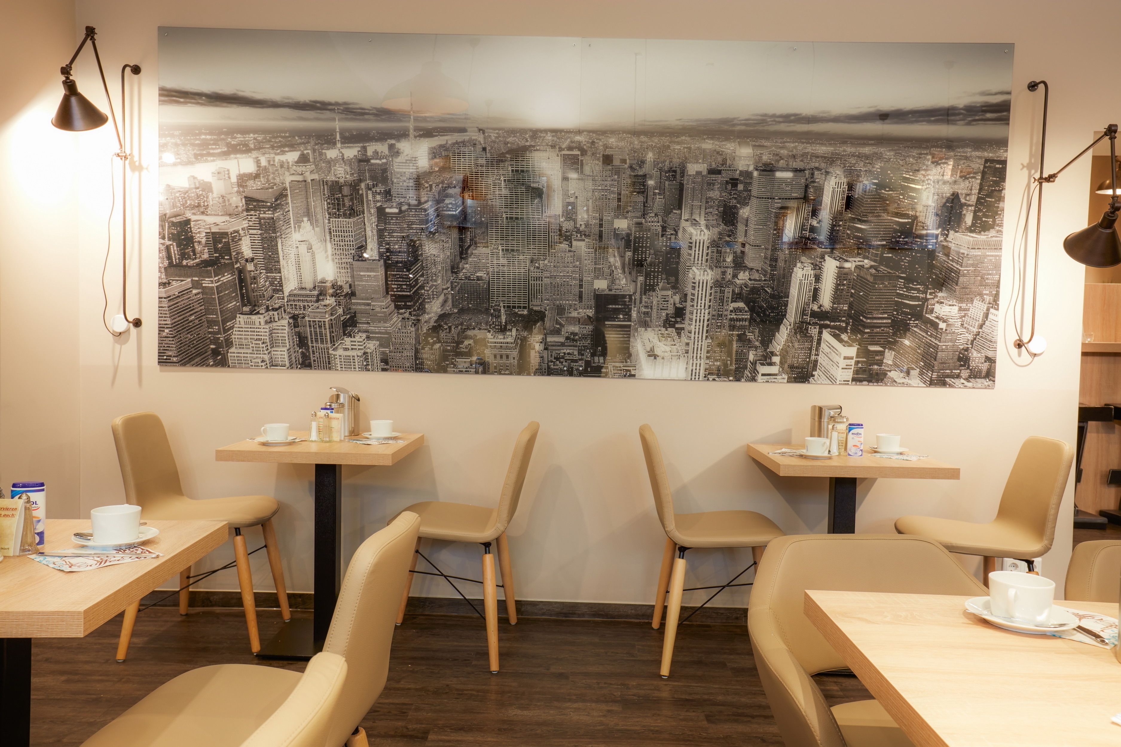 A modern cafe with a large cityscape mural on the wall, wooden tables, and comfortable chairs.