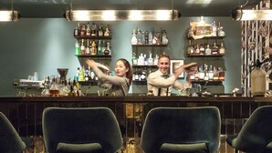 A bar area with shelves of liquor bottles, a bar counter, and two chairs in the foreground. - Manhattan Hotel (Frankfurt)