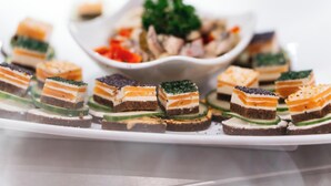 A white rectangular plate with several layered food items, including a green topping and a white creamy layer, arranged on a dark base. - City Park Hotel (Frankfurt an der Oder)