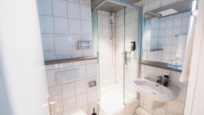 A modern bathroom with a glass-enclosed shower, a white sink, and a mirror above the sink. - City Park Hotel (Frankfurt an der Oder)