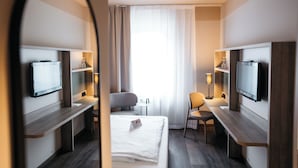 A hotel room with a bed, two bedside tables, a desk, a chair, a TV, and a mirror. - City Park Hotel (Frankfurt an der Oder)