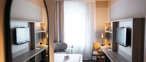 A hotel room with a bed, two bedside tables, a desk, a chair, a TV, and a mirror.