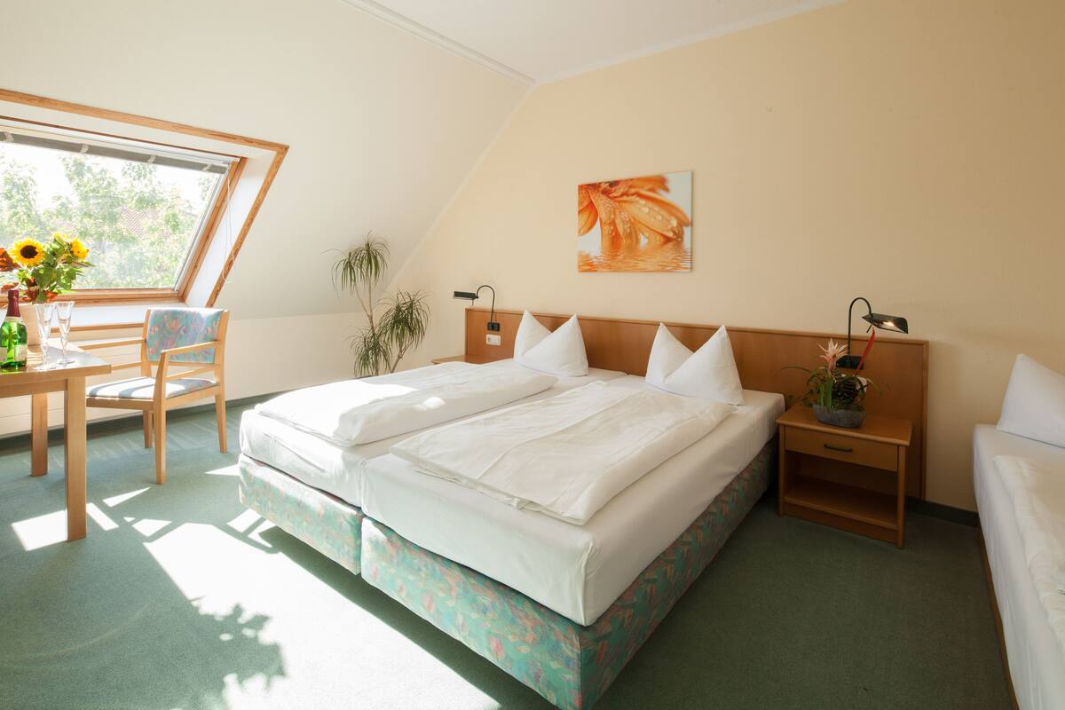 A bedroom with a large bed, a desk with a chair, a window, and a painting on the wall.