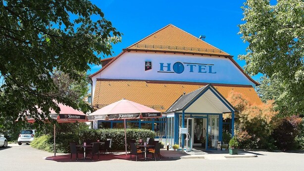 A hotel with a large sign, outdoor seating, and a covered entrance. - Apart Hotel Gera (Gera)