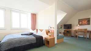 A bedroom with a bed, bedside table, lamp, chair, desk, TV, and artwork. - Apart Hotel Gera (Gera)