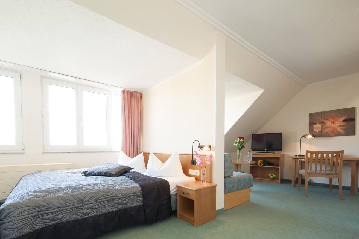 A bedroom with a bed, bedside table, lamp, chair, desk, TV, and artwork.