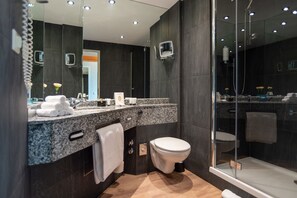 Une salle de bain moderne avec un comptoir en granit, des toilettes blanches, une douche à parois de verre et un grand miroir.