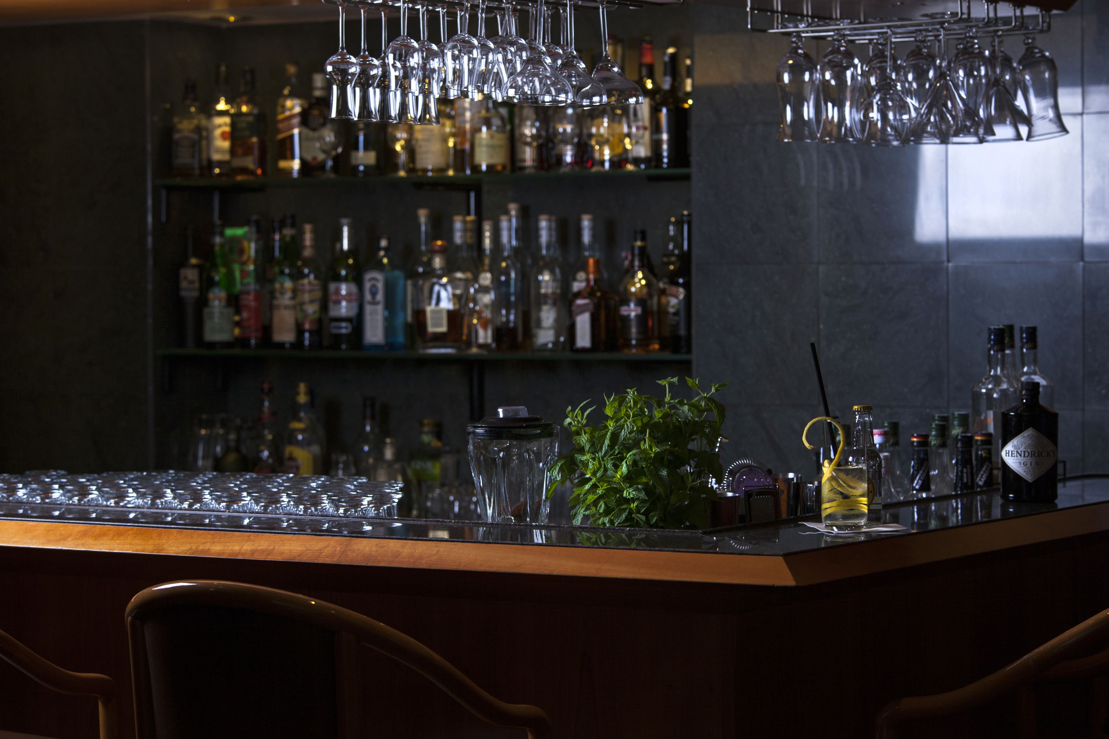 A bar area with shelves of liquor bottles, a bar counter, and hanging glasses.