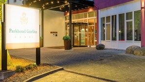 L’extérieur du Parkhotel Görlitz se distingue par son entrée moderne avec une porte en verre, un espace extérieur couvert agrémenté de guirlandes lumineuses et un panneau indicateur.