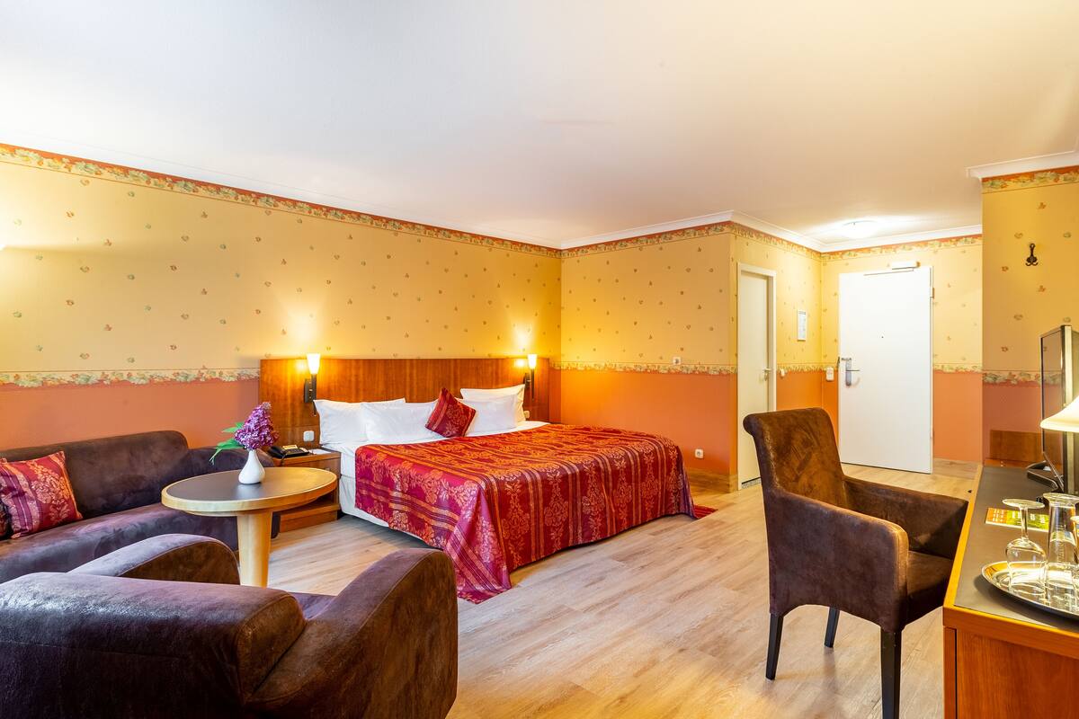 Habitación de hotel con una cama, dos sillones, una mesita redonda y un escritorio con una bandeja de objetos.
