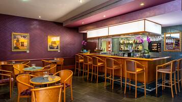 Uma área de bar com cadeiras e mesas de madeira, um balcão com adega e quadros nas paredes.