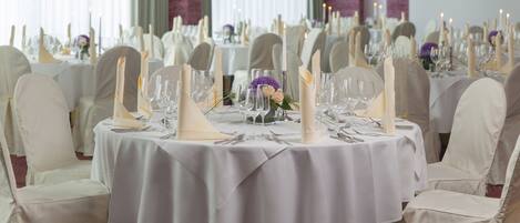 A banquet hall with round tables set for a formal event, featuring white tablecloths, candle centerpieces, and neatly arranged glassware.