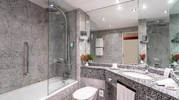 Un baño moderno con ducha de vidrio, una bañera independiente, un inodoro blanco y un tocador con encimera de granito.
