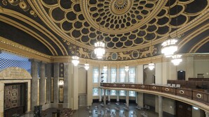 Un vaste hall doté d’un plafond richement décoré, de lustres et d’un balcon avec des sièges.