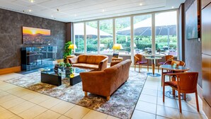 Un hall d’entrée spacieux, doté d’une grande fenêtre donnant sur l’extérieur, d’un coin salon confortable avec des canapés et des fauteuils, et d’un téléviseur à écran plat fixé au mur.