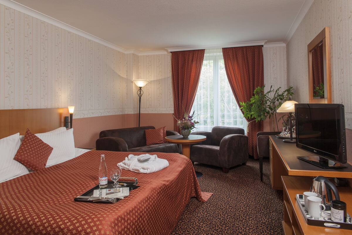 Habitación de hotel con una cama grande, un escritorio con televisor, un sofá y una pequeña mesa con un florero.