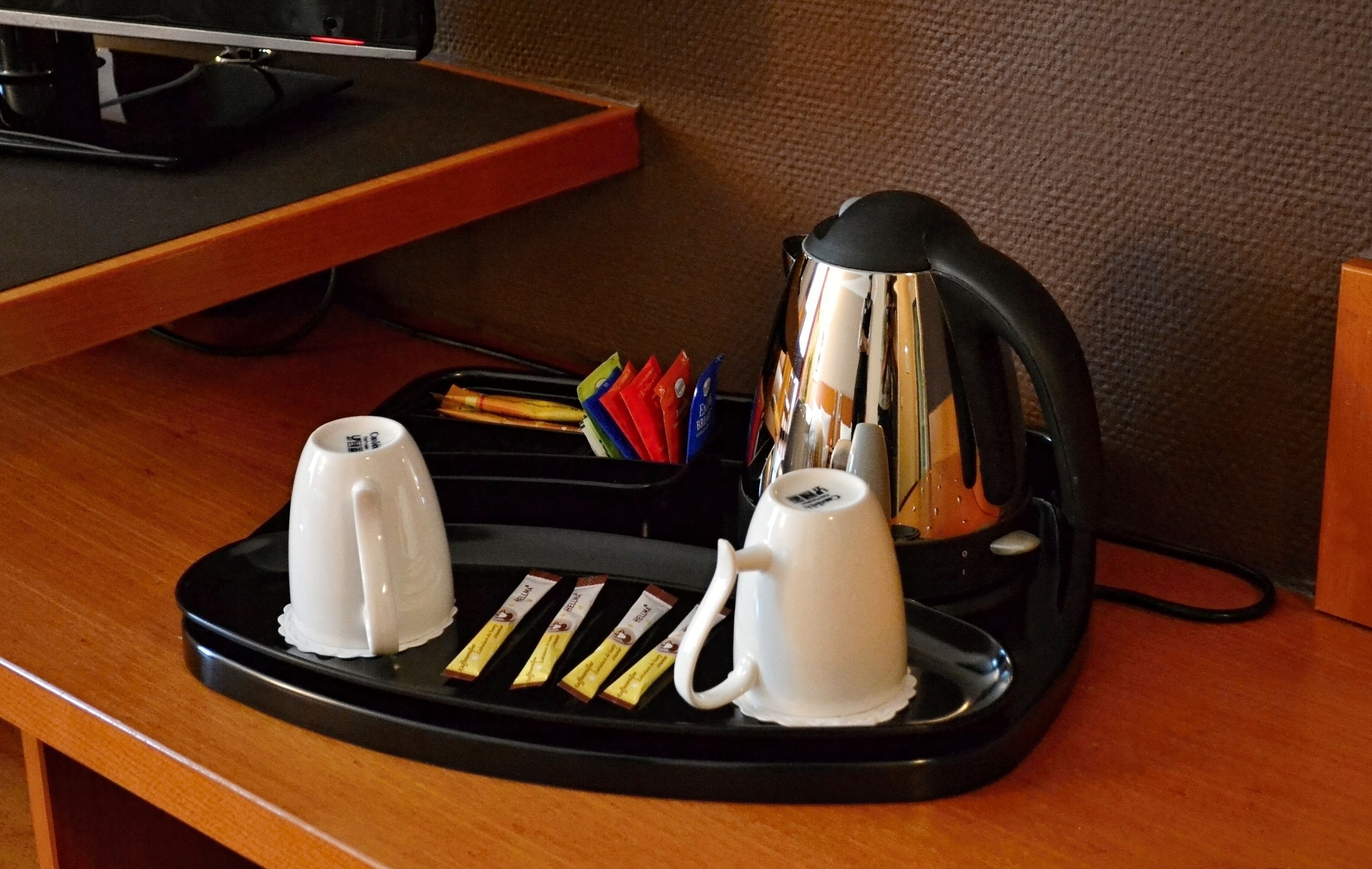 A coffee station with two white coffee cups, a black electric kettle, and a tray with coffee pods.