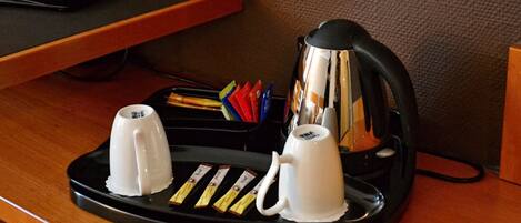 Una estación de café con dos tazas blancas, una tetera eléctrica negra y una bandeja con cápsulas de café.