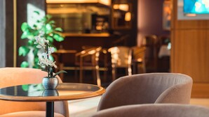 Un hall d’hôtel avec une table ronde, une orchidée en pot et un écran de télévision en arrière-plan.