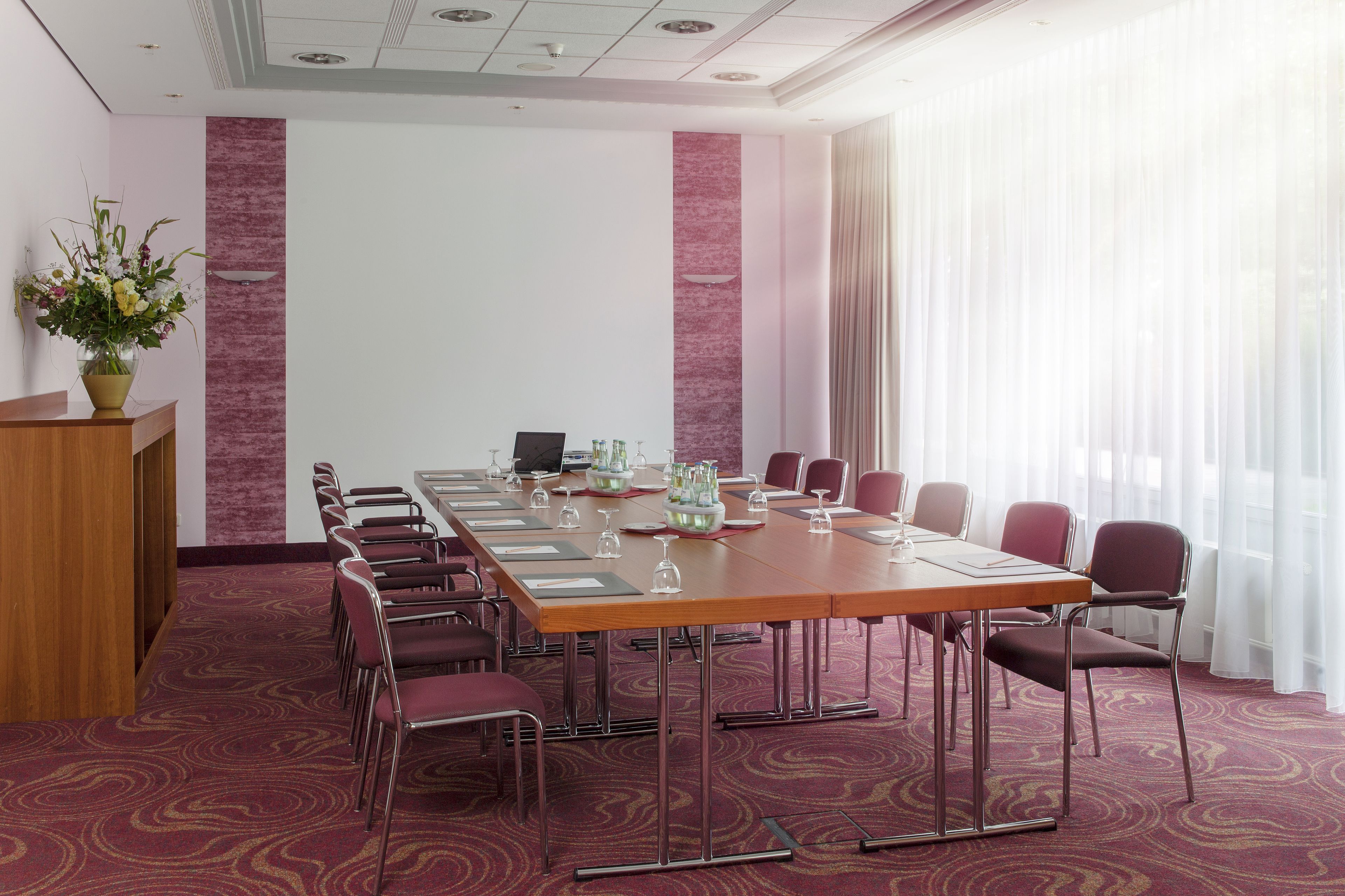 A conference room with a long table, chairs, a podium, and a projector screen.