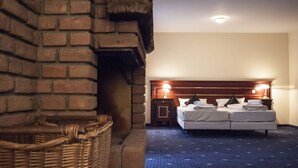 Habitación de hotel con chimenea de ladrillo, una cama con dos almohadas, una mesita de noche y una lámpara.